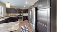 This single-story unit at 2220–2280 S 42nd St in Grand Forks, North Dakota, offers a well-designed layout with a cohesive modern aesthetic throughout. The open-concept living area is anchored by durable wood-look flooring, recessed lighting, and neutral walls that create a bright, welcoming atmosphere with ample room for both lounging and entertaining.

The kitchen is a standout feature, outfitted with rich dark cabinetry, stainless steel appliances including a French door refrigerator and electric range, and striking stone-look countertops. A kitchen island adds additional prep and dining space, while wood-look flooring ties the area seamlessly into the rest of the main living space.

The bedrooms are carpeted for comfort and include windows that bring in natural light. The primary bedroom connects to a well-appointed bathroom featuring dark cabinetry, stone-look countertops, a large vanity mirror, and a tall storage tower for added organization.

A second bathroom mirrors the same refined finishes. The dedicated laundry area includes an in-unit washer and dryer with overhead dark cabinetry for storage. A spacious walk-in closet with built-in shelving and hanging rods provides generous storage for the primary suite.