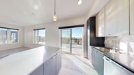 Located at 311 N Willson Ave in Bozeman, Montana, this contemporary 2-bedroom, 1-bathroom residence offers a thoughtfully designed single-level floor plan with clean lines and a modern aesthetic throughout. A welcoming entry hallway with crisp white walls and light wood-look flooring leads into the open-concept living and kitchen area, which serves as the heart of the home. The kitchen is a standout feature, centered around a large island with a sleek quartz countertop and dark navy cabinetry, complemented by two stylish pendant lights overhead. Two-toned cabinetry — light wood upper cabinets paired with dark lower units — lines the walls alongside full stainless steel appliances, including a range, microwave, and refrigerator, and a white subway tile backsplash adds a refined touch. Expansive floor-to-ceiling sliding glass doors and large windows flood the living area with natural light and provide direct access to a generous tiled outdoor terrace, which features glass panel railings and breathtaking panoramic views of the Bozeman skyline and surrounding landscape. The bathroom is elegantly appointed with a frameless glass walk-in shower, a floating vanity with an illuminated mirror, and light wood flooring. The bedrooms are bright and serene, with herringbone-patterned wood flooring and generous closet space.