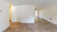 This single-floor residence offers a well-organized layout with distinct living, kitchen, bedroom, and bathroom areas. The open living and dining space features wood-look plank flooring that extends throughout the main areas, neutral cream-toned walls, and a textured ceiling. A standout feature is the dark-tiled fireplace, which anchors the living room alongside a large window that brings in natural light and views of surrounding greenery. A ceiling fan adds to the comfort of the space, and a sliding glass door provides access to a private outdoor patio area.

The kitchen is well-equipped with white cabinetry, gray laminate countertops, and white appliances including a refrigerator, electric range, and dishwasher. A window above the sink allows for natural light, and an adjacent utility area houses in-unit washer and dryer connections. The kitchen connects conveniently to the main living areas.

The two bedrooms are carpeted and share a similar layout, each featuring windows with outdoor views, baseboard heating, and ample closet space — one room includes a full-width sliding-door closet. The bathroom is finished with a tub-shower combination, a vanity with a gray countertop, and wood-look flooring, maintaining a clean, cohesive aesthetic throughout.