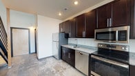 This two-story, 1-bedroom, 1.5-bathroom loft offers a thoughtfully designed living space that blends modern finishes with an open, airy layout. The kitchen is well-appointed with rich dark espresso cabinetry, granite countertops, stainless steel appliances including a refrigerator, dishwasher, microwave, and electric range, plus a breakfast bar with a built-in wine rack — ideal for casual dining and entertaining. Pendant lighting adds a stylish industrial touch above the bar area. The main living area features warm hardwood flooring and soaring vertical wall space, giving the home an expansive, loft-like feel. A staircase with metal railings leads to the upper-level loft, which serves as the bedroom and overlooks the main floor. A skylight on the upper level brings in natural light. The full bathroom is located on the main level and includes hardwood flooring, a tub/shower combination, a granite-topped vanity, and dark cabinetry consistent with the rest of the home. A convenient half-bathroom is also available, finished with a granite vanity countertop and a large mirror. Throughout the unit, cohesive design choices — including granite surfaces and dark cabinetry — create a polished, modern aesthetic.