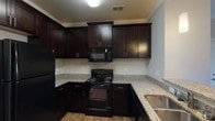 This single-story, two-bedroom, two-bathroom residence offers a thoughtfully designed layout with a blend of practical finishes throughout. The open living area features rich hardwood-style flooring, crown molding, and a large window that allows natural light to fill the space, creating a bright and welcoming atmosphere upon entry.

The kitchen is a standout feature, showcasing dark espresso cabinetry that extends to the ceiling, granite countertops, a double stainless steel sink, and black appliances including a range, microwave, and refrigerator. The wood-look flooring continues seamlessly through this space, complementing the kitchen's bold color palette.

Both bedrooms are generously sized and finished with plush carpeting, neutral-toned walls, ceiling fans, and windows with blinds that provide outdoor views and natural light. Each room offers a comfortable, functional environment suitable for varied uses.

The two bathrooms are finished with tile flooring and include tub-shower combinations and dark cabinetry for storage. A dedicated laundry room with washer and dryer hookups, built-in shelving, and tile flooring adds everyday convenience to the unit's practical design.