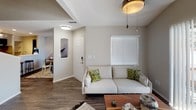 This two-story residence is designed with a neutral, contemporary aesthetic throughout. The main level features a living area with vaulted ceilings, a ceiling fan, and large windows that allow natural light to fill the space. A sliding glass door opens directly to an outdoor patio, extending the living area outdoors. The front entryway connects seamlessly to the living room, which flows toward the dining area and kitchen.

The kitchen is a standout feature, equipped with dark cabinetry, stainless steel appliances including a refrigerator, range, and microwave, as well as a white subway tile backsplash and light quartz countertops. A peninsula with bar-height seating provides additional dining and workspace. Hardwood-style flooring runs throughout the main level.

A bright staircase with a white railing leads to the upper floor, where carpeted bedrooms offer a softer feel. The primary bedroom includes vaulted ceilings, a walk-through closet, and an en-suite bathroom. The bathrooms feature quartz countertops, tub-shower combinations, and wood-look flooring. The overall palette of warm grays and whites creates a cohesive, modern ambiance throughout the home.