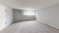 Located at 2800 Welsh Rd in Philadelphia's 19152 zip code, this one-bedroom, one-bathroom unit offers a practical and well-organized single-floor layout. The kitchen is a standout feature, showcasing crisp white shaker-style cabinetry, light granite-look countertops, a dark tile backsplash, and durable wood-look vinyl plank flooring. Stainless steel appliances — including a refrigerator, range, and microwave — provide a modern, functional cooking space with ample storage. The combined kitchen and living area creates an open, versatile space suited for everyday living. The bedroom is a generously proportioned room finished with soft carpeting, light gray walls, and a wide window fitted with vertical blinds that allows natural light to filter in. A baseboard heating system and wall-mounted A/C unit ensure year-round comfort. The bedroom connects directly to a dedicated walk-in closet, complete with dual hanging rods and carpeted flooring, offering substantial storage capacity. The full bathroom features a clean, white-tiled tub and shower combination, a standard toilet, and a streamlined design. Throughout the unit, neutral tones and functional finishes create a cohesive, move-in ready environment.