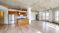 Located at 2101 Market St in the heart of Denver, CO, this urban loft-style residence showcases a compelling blend of industrial design and modern comfort. The open-concept living area is defined by dramatic exposed concrete ceilings with integrated track lighting and an overhead conduit rail, giving the space a distinctly contemporary, loft-inspired character. Light hardwood flooring runs throughout the main living areas, complementing the bright white walls and large windows that flood the interior with natural light and frame sweeping views of the surrounding Denver cityscape.

The well-appointed kitchen features warm-toned wood cabinetry, granite countertops, a classic white subway tile backsplash, stainless steel appliances, and a central island — all flowing seamlessly into the open living space. A curved alcove of floor-to-ceiling windows creates a sun-drenched living area with expansive city views on multiple sides.

The bedrooms offer plush carpeted flooring, clean white walls, and generous natural light through tall windows overlooking the city. Two full bathrooms are finished with granite-topped wood vanities, soaking tubs, and hardwood-style flooring. A walk-in closet provides ample storage. The unit occupies a single floor, offering a cohesive and functional layout ideal for urban living in Denver's vibrant Market Street corridor.