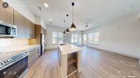 This well-appointed one-bedroom, one-bathroom residence in Durham, NC offers a thoughtfully designed open-concept floor plan that maximizes every square foot. Light wood-tone flooring flows seamlessly throughout, creating a warm and cohesive aesthetic across all living areas.

The kitchen is a standout feature, showcasing flat-front cabinetry in a rich wood finish, white quartz countertops, a white subway tile backsplash, and a full suite of stainless steel appliances including a refrigerator, range, and microwave. A generous central island with an integrated sink and pendant lighting serves as both a functional workspace and a natural gathering point, opening directly to the living area.

The living room is bright and airy, benefiting from multiple windows that frame outdoor views and a ceiling fan that enhances comfort. The bedroom is a comfortable retreat with its own ceiling fan, a large window providing natural light, and built-in shelving for added storage and display.

The bathroom is finished with large-format tile flooring, a wood-toned floating vanity with white countertops, a full tub-shower combination clad in classic white subway tile, and a well-lit vanity mirror. A dedicated closet completes the layout, offering practical storage solutions in this modern Durham residence.
