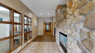 Located at Northwood Drive in Eagan, Minnesota, this single-floor clubhouse offers a well-appointed community gathering space designed for both relaxation and entertaining. The layout flows seamlessly across a generously sized floor plan, encompassing a living room, kitchen, and dining area.

The living room serves as the centerpiece of the clubhouse, anchored by a striking floor-to-ceiling river stone fireplace that adds a warm, rustic character to the space. Plush seating, a wall-mounted television, and large windows that invite natural light make this area ideal for casual gatherings. Tile flooring at the entry transitions to patterned carpeting throughout the main living areas.

The fully equipped kitchen features warm oak cabinetry, a mosaic tile backsplash, and a complete suite of appliances including a range, refrigerator, and microwave. An adjacent peninsula with bar-height seating bridges the kitchen and living area, making it well-suited for hosting events. Recessed lighting and multiple windows keep the kitchen bright and functional.

The dining area accommodates a round table with seating for several guests and benefits from large windows overlooking what appears to be an outdoor pool area, allowing natural light to fill the room. The overall ambiance is inviting and comfortable, combining practical amenities with warm, residential-style finishes throughout.