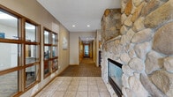 Located at Northwood Drive in Eagan, Minnesota, this single-floor clubhouse offers a well-appointed community gathering space designed for both relaxation and entertaining. The layout flows seamlessly across a generously sized floor plan, encompassing a living room, kitchen, and dining area.

The living room serves as the centerpiece of the clubhouse, anchored by a striking floor-to-ceiling river stone fireplace that adds a warm, rustic character to the space. Plush seating, a wall-mounted television, and large windows that invite natural light make this area ideal for casual gatherings. Tile flooring at the entry transitions to patterned carpeting throughout the main living areas.

The fully equipped kitchen features warm oak cabinetry, a mosaic tile backsplash, and a complete suite of appliances including a range, refrigerator, and microwave. An adjacent peninsula with bar-height seating bridges the kitchen and living area, making it well-suited for hosting events. Recessed lighting and multiple windows keep the kitchen bright and functional.

The dining area accommodates a round table with seating for several guests and benefits from large windows overlooking what appears to be an outdoor pool area, allowing natural light to fill the room. The overall ambiance is inviting and comfortable, combining practical amenities with warm, residential-style finishes throughout.
