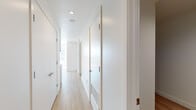 Located in the heart of Los Angeles at 1133 S Hope St, this modern single-floor residence offers a clean, contemporary aesthetic defined by an all-white palette, light wood flooring, and an abundance of natural light. The open layout is connected by a bright, well-proportioned hallway lined with flush white doors and recessed lighting, creating a seamless flow between spaces. The kitchen is a standout feature, outfitted with sleek flat-front cabinetry in a warm gray tone, white quartz countertops, a gray subway tile backsplash, and a full suite of stainless steel appliances including a French door refrigerator, electric range, built-in microwave, and dishwasher. The kitchen opens toward a generously sized living area bathed in sunlight from large floor-to-ceiling windows that frame views of the surrounding Los Angeles cityscape. The bedroom continues the bright, minimalist theme with expansive windows allowing ample natural light and urban views. The bathroom features a clean white vanity with an undermount sink, a large mirror with overhead lighting, and dark tile flooring that provides a subtle contrast to the otherwise light interior. Throughout the space, the consistent use of modern materials and neutral tones creates a cohesive, tranquil ambiance ideal for contemporary urban living.