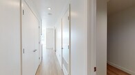 Located in the heart of Los Angeles at 1133 S Hope St, this modern single-floor residence offers a clean, contemporary aesthetic defined by an all-white palette, light wood flooring, and an abundance of natural light. The open layout is connected by a bright, well-proportioned hallway lined with flush white doors and recessed lighting, creating a seamless flow between spaces. The kitchen is a standout feature, outfitted with sleek flat-front cabinetry in a warm gray tone, white quartz countertops, a gray subway tile backsplash, and a full suite of stainless steel appliances including a French door refrigerator, electric range, built-in microwave, and dishwasher. The kitchen opens toward a generously sized living area bathed in sunlight from large floor-to-ceiling windows that frame views of the surrounding Los Angeles cityscape. The bedroom continues the bright, minimalist theme with expansive windows allowing ample natural light and urban views. The bathroom features a clean white vanity with an undermount sink, a large mirror with overhead lighting, and dark tile flooring that provides a subtle contrast to the otherwise light interior. Throughout the space, the consistent use of modern materials and neutral tones creates a cohesive, tranquil ambiance ideal for contemporary urban living.