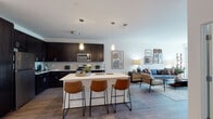 This single-floor residence on Progress Parkway in Schaumburg, Illinois, showcases a contemporary open-concept design that seamlessly connects the kitchen, dining, and living areas. The kitchen is a standout feature, outfitted with rich dark espresso cabinetry extending to the ceiling, crisp white quartz countertops, a full suite of stainless steel appliances including a gas range and built-in microwave, and a tile backsplash. A central island with an undermount sink provides additional workspace and seating for multiple bar stools, making it an ideal gathering spot.

The living area flows naturally from the kitchen and is bathed in natural light from large sliding glass doors that open to an outdoor space. Wood-style flooring runs throughout the main living areas, lending warmth and continuity to the open floor plan.

The bedroom offers a comfortable retreat with plush carpet, generous natural light from a window with outdoor views, and ample space for a full furniture arrangement. The bathroom features a dark-framed vanity mirror, white quartz countertop, and dark cabinetry that echoes the kitchen's design language. Throughout the residence, clean white walls and consistent finishes create a cohesive, modern aesthetic.