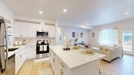 This well-designed one-bedroom, one-bathroom unit offers a thoughtful layout across a single floor, making efficient use of its space. The open-concept kitchen and living area serves as the heart of the home, anchored by a large center island with a quartz countertop — ideal for dining or casual entertaining. The kitchen is outfitted with white shaker cabinetry, open shelving, stainless steel appliances including a refrigerator, dishwasher, microwave, and range, all set against light hardwood flooring that flows seamlessly throughout. The living room is bright and airy, benefiting from natural light through windows and a glass door that opens to an outdoor area. A dedicated office provides a quiet, versatile space with a clean, minimalist feel accented by hanging shelving. The bedroom is a serene retreat with crisp white walls, a closet with built-in rod storage, and warm wood floors. The bathroom features decorative patterned tile flooring, a white vanity, and a shower-tub combination. A private in-unit laundry room houses a full-size washer and dryer. The home's consistent palette of white walls, light wood floors, and modern fixtures creates a cohesive, inviting atmosphere throughout.