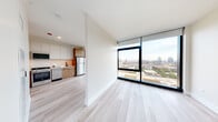 Located in Chicago's vibrant West Loop neighborhood, this modern high-rise unit at 1125 W Van Buren Street offers a sleek, contemporary living experience defined by clean lines and premium finishes throughout. Light hardwood flooring flows seamlessly across the entire unit, complementing the bright, neutral palette of the walls and ceilings.

The open-concept living and dining area is anchored by dramatic floor-to-ceiling windows with bold black frames, flooding the space with natural light and offering sweeping panoramic views of the Chicago skyline and surrounding cityscape. The kitchen is thoughtfully designed with a combination of white upper cabinetry and warm wood-toned lower cabinets, complemented by a neutral tile backsplash, stainless steel appliances including a gas range and refrigerator, and ample counter space.

The bedroom continues the floor-to-ceiling window motif, maximizing both natural light and city views, while roller shades provide privacy as needed. A well-organized hallway features built-in storage and closet space, enhancing functionality. The bathroom is finished with elegant marble-style tile flooring, a floating wood-toned vanity, an undermount sink, and a large mirror, delivering a refined, spa-like aesthetic. The overall ambiance is modern, airy, and sophisticated.