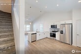 Located at 9000 Little Palm Way in Venice, FL, this two-story home offers a well-designed layout across two floors, with the main living areas on the ground level and additional bedrooms above. The open-concept main floor is anchored by a bright, airy living and dining area featuring soaring vaulted ceilings and recessed lighting that amplify the sense of space. The contemporary kitchen is outfitted with white shaker cabinetry, a gray tile backsplash, stainless steel appliances including a side-by-side refrigerator, electric range, and built-in microwave, along with a peninsula sink that seamlessly connects to the living area. Light wood-look flooring flows throughout, lending a clean, cohesive aesthetic. Each of the three bedrooms is well-proportioned, featuring ceiling fans, natural light from multiple windows, and easy access to closet space. The three bathrooms are finished in a neutral palette, with one featuring a tiled tub-surround and white vanity with brushed nickel fixtures. A dedicated laundry room houses a full-size washer and dryer. The exterior features a fully fenced, private backyard with a white vinyl privacy fence and a small lawn area, ideal for outdoor enjoyment. A utility room and ample hallway space add further practicality to this move-in-ready home.