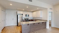 This thoughtfully designed 3-bedroom, 2-bathroom single-floor residence offers a comfortable and functional layout ideal for everyday living. The open-concept kitchen and living area serves as the heart of the home, featuring a large peninsula with a light quartz countertop, dark wood-toned cabinetry, stainless steel appliances including a refrigerator, electric range, and built-in microwave, and recessed lighting throughout. Light wood-style flooring flows seamlessly from the kitchen into the adjoining living area, which benefits from natural light through a bright window. The primary bedroom is generously sized and includes its own walk-in closet with built-in shelving and hanging rods, carpeted flooring, and two windows that invite ample natural light and outdoor views. The two additional bedrooms are well-proportioned—one features light wood-style flooring with a large window, while the other is carpeted with dual windows offering garden views. Both bathrooms are clean and functional, with one featuring a full soaking tub and shower combination with built-in shelving, wood-look tile flooring, and a vanity with dark cabinetry. Throughout the residence, neutral wall tones, white trim, and textured ceilings create a bright, cohesive, and move-in-ready atmosphere.
