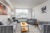 This single-floor residence offers a thoughtfully designed layout that blends functionality with modern style. The open-concept kitchen and living area forms the heart of the home, anchored by a spacious island with a white quartz countertop, an undermount sink, and pendant lighting in striking blue glass. The kitchen is fully equipped with stainless steel appliances — including a range, microwave, dishwasher, and refrigerator — complemented by warm wood cabinetry and light wood-look flooring. A ceiling fan overhead and a large window with horizontal blinds flood the living area with natural light, while a sliding door provides access to a balcony with neighborhood views. The living room features a welcoming layout with ample space for seating and a decorative accent wall. Two bedrooms offer comfortable retreats, each carpeted and naturally lit through windows overlooking the surrounding neighborhood. The bathroom includes a full soaking tub with classic white tile surround and chrome fixtures. Throughout the residence, neutral walls, clean lines, and consistent finishes create a cohesive and inviting atmosphere suited for everyday living.