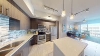 This well-appointed one-bedroom, one-bathroom unit offers a thoughtfully designed single-floor layout that maximizes every inch of its compact footprint. The open-concept kitchen and living area serves as the heart of the space, where a sleek kitchen island with seating anchors the room. Dark wood cabinetry, a multicolored tile backsplash, stainless steel appliances—including a range, microwave, and refrigerator—and pendant lighting above the island combine for a modern, polished aesthetic. Light-toned tile flooring runs throughout the main living areas, enhancing the sense of openness. The adjoining living and dining area features a ceiling fan, light-toned flooring, and ample room for both a seating arrangement and dining table. The bedroom is a cozy retreat with direct access to the full bathroom, which includes a soaking tub and shower combination, dark wood vanity with white countertop, and tile flooring. A dedicated walk-in closet off the bedroom provides wire shelving and generous storage capacity. Track lighting and pendant fixtures throughout the unit contribute to a bright, contemporary ambiance.