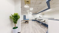 Located at 2444 E Maple Ave in Burlington, NC, this single-floor commercial space offers a generously open and flexible layout designed to accommodate a variety of uses. The interior is finished with light-toned luxury vinyl plank flooring that runs throughout, creating a clean, contemporary look. Crisp white walls are accented by a bold navy-blue horizontal band and matching blue baseboard trim, adding a cohesive and polished design element to the space.

The main area is anchored by a pool table with a blue felt surface, making it well-suited for recreational or lounge-style programming. High-top tables with modern bar stools are arranged along one side, providing a social gathering area. Pendant dome lights hang from the drop-tile ceiling, complementing the recessed and fluorescent lighting that ensures the space is well-lit throughout.

A stepped platform area with a built-in ledge adds architectural dimension and defines distinct zones within the open floor plan. A glass-windowed partition near the entrance provides separation while maintaining visibility across the space. Decorative potted plants are positioned near the entry, lending a welcoming touch. A steel-frame entry with glass-panel doors leads to a connecting corridor, completing the functional and thoughtfully designed layout of this Burlington commercial property.