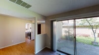 Located in Portland, Oregon, this two-story residence on NE Lapine Way offers a practical and well-organized layout across two levels. The main living area features hardwood-style flooring and large sliding glass doors that flood the space with natural light while providing direct views of the surrounding greenery and outdoor patio area. A second set of sliding glass doors on the lower level similarly opens to the outdoors, extending the living space seamlessly.

The kitchen is efficiently designed with white upper cabinetry, gray lower cabinets, white countertops, a stainless steel sink, and a full suite of stainless steel appliances including a range and dishwasher. The kitchen connects conveniently to the dining and living areas, which share the same warm hardwood-style flooring. Textured ceilings are consistent throughout the interior.

The bedrooms are carpeted and feature closets and windows that provide natural light. The bathroom is clean and modern, with a wide vanity, white countertop, large mirror, and hardwood-style flooring. The home also includes an attached garage with a window and utility infrastructure. A staircase connects the two floors, creating a cohesive multi-level living experience well-suited to the Pacific Northwest setting.