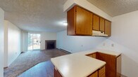 This single-floor unit offers a practical and functional layout across several well-defined spaces. The open-concept kitchen and living area form the heart of the unit, where the kitchen features warm medium-toned wood cabinetry—both upper and lower—with white laminate countertops, wood-look hard flooring, and a full suite of white appliances including a refrigerator, dishwasher, and range with overhead ventilation. A peninsula counter separates the kitchen from the adjacent living area, providing a natural transition between the two spaces.

The living room is carpeted and centers around a tile-surround fireplace, adding a focal point to the room. A sliding glass door allows natural light to fill the space and offers views of the surrounding outdoor greenery. Baseboard heating runs along the perimeter walls throughout the unit, supplemented by a wall-mounted air conditioning unit in the bedroom.

The bedroom is generously proportioned with plush carpeting, a textured ceiling, and a window framing a lush tree view. The full bathroom includes a tub-shower combination with tile surround, a single vanity with wood cabinetry, and a mirrored medicine cabinet. Additional doors along the hallway provide access to closets and utility areas, completing this well-organized layout.