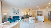 Located at 313 Cantabria Trail in Bradenton, Florida, this two-story home presents a bright, coastal-inspired interior designed for comfortable Florida living. The main floor opens into a spacious, light-filled living area finished with large-format tile flooring and neutral white walls that enhance the airy atmosphere. A stylish geometric chandelier anchors the dining area, while the adjoining living room features plush seating, a glass coffee table, and coordinated blue and white coastal accents. A convenient half bath with a pedestal sink is tucked near the entry.

The kitchen is thoughtfully designed with white shaker cabinetry, granite countertops, stainless steel appliances, and a peninsula with seating — ideal for casual dining. In-unit laundry is also accessible from this level.

Upstairs, the bedrooms are carpeted and filled with natural light from windows dressed with blinds and curtains. The primary suite includes an en-suite bathroom with tile flooring, a granite-topped vanity, a glass-enclosed shower, and a walk-in closet. An additional full bathroom features floor-to-ceiling tile surrounding a soaking tub and shower combination, offering a clean, classic finish throughout.