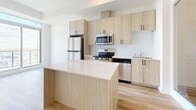 Located at 2475 Old Bronte Rd in Oakville, Ontario, this thoughtfully designed one-bedroom, two-bathroom unit offers a clean, modern aesthetic with light hardwood flooring and crisp white walls throughout. The welcoming entrance leads into an open-concept living area bathed in natural light from expansive floor-to-ceiling windows that also frame views of the surrounding landscape.

The kitchen is a standout feature, equipped with light wood cabinetry accented by matte black hardware, a white quartz island/peninsula, subway tile backsplash, and a full suite of stainless steel appliances including a refrigerator, range, microwave, and dishwasher. The layout maximizes functionality while maintaining a bright, airy feel.

The primary bedroom offers a comfortable, well-proportioned retreat, complemented by ample closet space — with three closets found throughout the unit. A versatile den provides additional flexibility for a home office or guest space. The balcony extends the living area outdoors, offering a pleasant space to enjoy fresh air and views.

Both bathrooms are finished in clean white tile. One features a soaker tub-shower combination, while the combined bathroom and laundry space includes a walk-in shower with dark-framed glass door. Together, they deliver practical convenience in a polished, modern package.