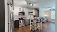 Located at 2470 Cheshire Bridge Rd NE in Atlanta, GA, this well-designed unit offers a smart, efficient layout that maximizes every square foot across a single floor. Warm hardwood-style flooring flows seamlessly throughout, creating a cohesive and inviting atmosphere.

The kitchen is a standout feature, outfitted with stainless steel appliances including a refrigerator, range, dishwasher, and microwave. Two-tone cabinetry pairs dark wood lower cabinets with crisp white uppers, complemented by a classic subway tile backsplash and open shelving. A built-in breakfast bar provides convenient casual dining space. Track lighting overhead adds both function and a contemporary flair.

The kitchen opens directly into the living area, which benefits from a large window that fills the room with natural light and offers a view of surrounding greenery. A ceiling fan adds comfort, and the neutral wall tones create a calm, versatile backdrop.

The bathroom is thoughtfully appointed with a dark wood vanity, white quartz countertop, a large framed mirror, and a glass-enclosed walk-in shower finished with white subway tile. A dedicated closet provides practical storage to round out the unit's functional offerings.
