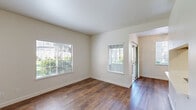 This efficiently designed one-bedroom, one-bathroom residence offers a thoughtful layout that maximizes every square foot across a single floor. The combined kitchen and living area serves as the heart of the home, featuring warm wood-toned cabinetry, white countertops, and white appliances including a refrigerator and electric range with overhead ventilation. Rich, dark hardwood-style flooring runs throughout the main living spaces, lending warmth and continuity to the open feel.

The living and dining areas are bathed in natural light through multiple windows fitted with horizontal blinds, with a sliding glass door providing additional brightness and outdoor access. A dedicated dining space features a stylish pendant light fixture, positioned conveniently adjacent to the kitchen.

The bedroom offers plush carpeting underfoot, a ceiling fan with light fixture, and a window with garden views, creating a comfortable and restful retreat. A dedicated closet provides practical storage. The full bathroom includes a wood-toned vanity with white countertop, a large mirror with overhead lighting, and a shower-tub combo with frosted glass enclosure. Neutral, light-toned walls throughout the residence create a clean, airy ambiance that complements the warm flooring and cabinetry accents.