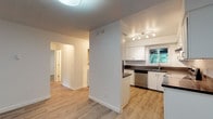 This single-floor unit offers a clean, updated interior with a consistent design aesthetic throughout. Light-toned laminate wood flooring runs through the living areas, bedrooms, kitchen, and bathroom, providing visual continuity across the space. Textured ceilings are present throughout, adding a classic architectural detail.

The kitchen is well-appointed with white shaker-style cabinetry, dark countertops, stainless steel appliances including a dishwasher, a stainless steel sink, and track lighting overhead. A window above the sink allows natural light to filter in and provides views of surrounding greenery.

The living area is generously sized and features large sliding glass doors with vertical blinds, opening to an outdoor balcony and framing views of mature trees. Baseboard heating runs along the perimeter walls. A second, equally spacious living or dining area connects directly to the kitchen via a hallway.

The bedrooms are bright and well-proportioned. One features a wide sliding-door closet system with built-in shelving and hanging space, while others include ceiling fans, windows with outdoor views, and baseboard heaters. The bathroom is finished with wood-toned cabinetry, a white tub-shower combination with tiled surround, and brushed nickel fixtures.