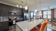 This well-appointed single-floor residence offers a thoughtfully designed open-concept layout that seamlessly connects the main living areas. The kitchen is a standout feature, showcasing dark espresso cabinetry, a mosaic tile backsplash, stainless steel appliances, and a generous granite island with pendant lighting and bar seating — ideal for both casual dining and entertaining. The kitchen flows naturally into the dining area and a comfortable living room, which benefits from large windows offering views of the surrounding area and access to a private balcony. Rich wood-style flooring extends throughout the main living spaces, complemented by plush carpeting in the bedrooms. The primary bedroom is well-sized with ample natural light, while the en-suite bathroom features granite countertops, dark cabinetry, a walk-in closet, and a shower. A second bedroom offers a cozy, private retreat, and a second full bathroom provides added convenience. Ceiling fans in the living area and recessed and track lighting throughout contribute to the space's functional, modern ambiance. The neutral color palette and clean architectural lines create a cohesive, contemporary aesthetic across the entire residence.