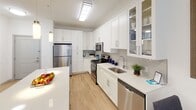 Located at 1140–1198 Market St in Dresher, Pennsylvania, this single-floor residence offers a thoughtfully designed, open-concept layout with a clean, contemporary aesthetic throughout. The living area is bright and welcoming, anchored by light hardwood-style flooring, neutral walls, and floor-to-ceiling sliding glass doors dressed with sheer vertical blinds that invite an abundance of natural light. The space provides a comfortable and airy atmosphere ideal for both relaxing and entertaining.

The kitchen is a standout feature, outfitted with crisp white shaker-style cabinetry, quartz countertops, a herringbone tile backsplash, and a full suite of stainless steel appliances including a refrigerator, range, over-the-range microwave, and dishwasher. Pendant lighting and a central island add both functionality and style to this well-equipped space.

The bedroom is a serene retreat, featuring plush carpeting, a large window with horizontal blinds that filter natural light, and ample space for a full bedroom suite. The room is finished with neutral tones that create a calm and restful environment.

The bathroom is elegantly appointed with a floating white vanity, quartz countertop, a large framed mirror, recessed lighting, and a walk-in shower finished with floor-to-ceiling marble-look tile. Tasteful grey floor tiles and refined fixtures complete this polished space.
