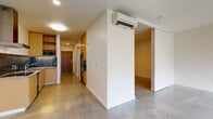 This single-floor space showcases a clean, contemporary design defined by polished concrete floors that run throughout and bright white walls that lend a cohesive, modern aesthetic. The open-concept layout connects the kitchen and living areas seamlessly, promoting a sense of spaciousness.

The kitchen is thoughtfully outfitted with flat-front light wood cabinetry — both upper and lower — paired with grey countertops and a sleek dark metal backsplash. Stainless steel appliances include a refrigerator, wall oven, dishwasher, electric cooktop, and built-in microwave, along with a range hood overhead. A corridor from the kitchen leads directly to the entry door.

The living area is a notable highlight, featuring a generous bank of wood-framed windows that frame views of the surrounding cityscape and greenery, flooding the space with natural light. A wall-mounted mini-split system provides climate control throughout.

The bathroom features subway tile surrounding a full soaking tub with shower, complemented by a wood-front vanity and concrete flooring. A dedicated laundry area accommodates a stacked washer and dryer unit, adding practical convenience to the overall layout.