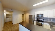 This single-floor residence offers a thoughtfully designed layout that balances functionality and comfort. The kitchen serves as a standout feature, showcasing stainless steel appliances including a refrigerator, electric range, and over-the-range microwave. White cabinetry with ample storage lines the walls, complemented by a gray subway tile backsplash and dark laminate countertops that extend to a peninsula, ideal for casual dining or meal prep. Wood-look flooring runs throughout the main living and kitchen areas, adding warmth and continuity to the space.

The open layout connects the kitchen seamlessly to the living area, which benefits from access to a patio or balcony through vertical blinds, allowing natural light to filter in. A built-in pantry or shelving unit provides additional storage near the kitchen, while multiple interior doors lead to the private areas of the home.

The bedrooms feature plush wall-to-wall carpeting and are each equipped with ceiling fans for year-round comfort. Windows dressed with blinds allow natural light into each room while maintaining privacy. The neutral, warm-toned walls throughout the unit create a clean and inviting atmosphere. The overall design is practical and move-in ready, offering a comfortable living environment across its well-organized floor plan.