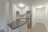 Located at 444 Victoria Rd N in Guelph, Ontario, this efficiently designed unit makes excellent use of its compact footprint across a single floor. The open-concept layout seamlessly connects the kitchen and living area, creating a cohesive and functional living space. Light-toned laminate flooring runs throughout, lending a clean, modern aesthetic.

The kitchen is well-appointed with crisp white shaker-style cabinetry, a classic white subway tile backsplash, dark granite countertops, and a peninsula that doubles as a breakfast bar. Stainless steel appliances — including a range, over-the-range microwave, and refrigerator — complete the space with a polished finish.

The living area is bright and airy, benefiting from a large sliding glass door that floods the room with natural light and provides direct access to the private balcony, which overlooks a treed outdoor setting. A baseboard heating system runs along the perimeter, ensuring year-round comfort.

The bathroom features floor-to-ceiling white subway tile surrounding a full soaker tub and shower combination, complemented by chrome fixtures for a timeless, clean look. Overall, the unit presents a cohesive design with consistent white tones, modern finishes, and thoughtful use of space throughout.