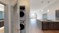 This contemporary single-floor residence showcases a clean, modern design with an emphasis on functionality and style throughout. The open-concept kitchen is a standout feature, boasting soaring ceilings, dark-toned cabinetry with a tile backsplash, stainless steel appliances including a refrigerator, microwave, and dishwasher, and a generous peninsula with a light quartz countertop and undermount sink. Elegant pendant lighting adds a refined touch overhead. Light wood-look flooring runs through the main living areas, lending warmth and continuity to the open layout. A dedicated in-unit laundry closet with stacked washer and dryer units is conveniently tucked behind louvered doors, seamlessly integrated into the space. The bedroom features plush carpeting, tall ceilings, and a bright window offering views of the surrounding neighborhood and skyline. A second sun-drenched room with wood-look flooring opens to an outdoor area through a glass door and features a large picture window with sweeping views of trees and distant hills. The bathroom is tastefully finished with large-format tile flooring, a wood-grain floating vanity, a framed mirror, and a tub-shower combination. Every element of this residence reflects a thoughtful, contemporary aesthetic designed for comfortable, stylish living.
