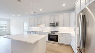 This well-appointed 2-bedroom, 2-bathroom residence spans a single floor and features a clean, modern aesthetic defined by light hardwood flooring, crisp white walls, and recessed lighting throughout. The open-concept kitchen and living area serves as the heart of the home, showcasing a generous central island with a white quartz countertop, shaker-style cabinetry in soft grey and white tones, a full suite of stainless steel GE appliances including a range, microwave, and refrigerator, and a classic white subway tile backsplash. Pendant lighting above the island adds a stylish finishing touch. The living room offers an expansive wall of windows fitted with roller shades, filling the space with natural light and providing views of the surrounding community. Both bedrooms are well-sized, with the primary bedroom featuring a large walk-in closet equipped with wire shelving systems for ample storage. The primary bathroom is elegantly finished with marble-look tile flooring, a dual-sink vanity with a white quartz countertop, shaker-style cabinetry, and a large framed mirror with wall sconce lighting. A dedicated laundry room houses a full-size GE front-loading washer and dryer. The unit offers a well-balanced blend of functionality and modern design throughout.