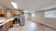 Located at 1764 N Leverett Ave in Fayetteville, Arkansas, this efficiently designed single-floor unit offers a practical and comfortable layout. The open-concept living and kitchen area forms the heart of the space, filled with natural light from multiple windows dressed with white blinds. A ceiling fan overhead enhances airflow and comfort throughout the main living area, which features light hardwood-style flooring that flows seamlessly across the entire unit.

The kitchen is well-appointed with warm honey-toned wooden cabinetry providing generous upper and lower storage, complemented by clean white countertops. Stainless steel appliances include a gas range, built-in microwave, dishwasher, and a full-size refrigerator, all illuminated by a bright overhead fluorescent fixture. A stainless steel sink with a modern faucet anchors the countertop workspace.

The bathroom features a full-size soaking tub with a clean white surround, offering a simple and functional design. The unit also includes four closets, providing exceptional storage capacity relative to the overall footprint. A hallway connects the various areas of the unit, contributing to a logical and easy-to-navigate floor plan. The textured ceiling throughout adds a classic finishing detail to this move-in ready space.