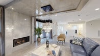 This thoughtfully designed single-floor space makes a striking first impression with its luxurious living area, where a bold, cascading crystal chandelier suspended from a polished, reflective ceiling panel serves as the undisputed focal point. The living area is anchored by a modern linear fireplace set within a smooth concrete-finish wall, flanked by floor-to-ceiling glass doors that flood the space with natural light and offer views of the lush outdoor surroundings. A striking artistic wall mural depicting a mountain landscape adds depth and visual interest, complementing the refined yet approachable aesthetic throughout. Light wood-look tile flooring runs seamlessly across the space, unifying the open-plan layout.

The kitchen is clean and functional, outfitted with crisp white cabinetry, quartz countertops, and stainless steel appliances including a range and dishwasher. A utility area adjacent to the kitchen provides additional cabinetry and laundry hookups for practical convenience.

Beyond the main living zone, a generously proportioned open area with recessed lighting and neutral walls offers flexible use, with a dedicated dining space visible nearby. Throughout, the design balances contemporary elegance with functionality, creating a welcoming and versatile environment suited for a variety of uses.