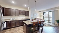 Located at 130 Fifth St SW in Rochester, Minnesota, this 1-bedroom, 1-bathroom residence offers a thoughtfully designed open-concept layout with modern finishes throughout. The kitchen is a standout feature, showcasing rich dark-espresso cabinetry, light granite countertops, a full suite of stainless steel appliances, and a central island with bar seating — ideal for both meal prep and casual dining. Warm wood-look flooring flows through the kitchen and living areas, adding a cohesive, contemporary feel. The living room is bright and inviting, anchored by large floor-to-ceiling sliding glass doors that open to a private balcony with sweeping views of the Rochester skyline. The bedroom is carpeted for comfort and features a large window that continues the city view, along with access to a dedicated closet area. The bathroom is clean and well-finished with tile flooring and a full tub-shower combination. A dedicated laundry area with a stacked washer and dryer provides added convenience. The overall ambiance is modern and functional, with neutral tones and quality materials creating a polished, move-in-ready home suited for urban living.