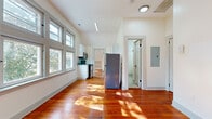 This single-floor space blends classic character with modern updates throughout its thoughtfully designed layout. Rich, warm-toned hardwood floors run throughout the main living areas, catching natural light and adding a sense of warmth and continuity to the space.

The kitchen is efficiently designed in a galley style, featuring white shaker cabinetry, granite countertops, and a full suite of stainless steel appliances including a refrigerator, dishwasher, range, and microwave. A window over the counter allows natural light to pour in, keeping the space bright and functional. An electrical panel is conveniently accessible nearby.

The living and sleeping areas benefit from vaulted ceilings that add a sense of openness and volume. One room stands out with distinctive built-in wall niches framing a central window — a charming architectural detail that adds character and visual interest. Another room features a sloped ceiling consistent with the roofline, paired with a window overlooking greenery, creating a cozy, tucked-in atmosphere.

A bank of multi-pane windows in one room frames lush tree views, filling the space with soft, diffused light. The bathroom area features neutral stone-look tile flooring and crisp white walls, accessed through a door with a decorative vintage-style handle, offering a subtle nod to the building's classic origins.