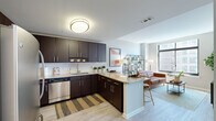 This thoughtfully designed one-bedroom, one-bathroom residence offers a smart, efficient layout across a single floor. The open-concept kitchen and living area serves as the heart of the unit, where rich dark-espresso cabinetry, granite countertops, a white subway tile backsplash, and stainless steel appliances—including a dishwasher, range, microwave, and full-size refrigerator—combine to create a sleek, functional kitchen. A peninsula with bar seating provides an ideal space for casual dining and entertaining. Light wood-style flooring runs throughout, lending warmth and visual continuity to the space. The living area is bathed in natural light from large, floor-to-ceiling windows with urban views, creating an airy and welcoming atmosphere. A hallway connects the main living space to the private bedroom, which features oversized windows with outdoor views, neutral tones, and ample room for a full bedroom suite. The bathroom is finished with granite countertops, dark cabinetry matching the kitchen, and a tub-shower combination with tile flooring. A dedicated closet and hallway provide practical storage solutions. The overall ambiance is modern and clean, with consistent finishes and a neutral palette that makes the space feel bright and move-in ready.