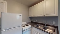 Located at 2143 Winslow Dr in Columbus, Ohio, this single-floor unit offers a practical and straightforward layout across several distinct areas. The kitchen is efficiently designed, featuring white cabinetry with raised-panel doors, dark laminate countertops, a double-basin stainless steel sink, a white electric coil-top range, and a full-size refrigerator — providing all the essentials in a compact, well-organized space. The kitchen transitions to a wood-look flooring that contrasts with the plush carpeting found throughout the living and sleeping areas. The main living space is open and versatile, benefiting from a large window that draws in natural light and offers views of the surrounding greenery. Wall-mounted air conditioning units are present in multiple rooms, ensuring climate control throughout the unit. An additional carpeted room with multiple windows provides flexible use as a bedroom or secondary living space. The bathroom is equipped with a walk-in shower, a soaking tub, a vanity sink, and wood-look flooring, finished with neutral gray walls and chrome fixtures. Textured ceilings are consistent throughout the unit, and neutral gray wall tones create a calm, cohesive atmosphere from room to room.