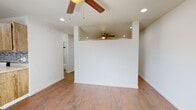 Located at 3125 N Alvernon Way in Tucson, Arizona, this single-floor unit offers a clean, functional layout with consistent design choices throughout. The main living area is bright and open, featuring warm wood-look flooring that extends across the entire space, crisp white walls, and multiple ceiling fans that aid in climate control alongside a wall-mounted AC unit. Recessed lighting is installed throughout, providing even illumination across each area. A partial dividing wall adds subtle architectural definition between living zones while maintaining an open feel. The kitchen is efficiently designed, equipped with natural wood cabinetry, a stainless steel sink, a coil-burner electric range, a full-size refrigerator, and an overhead microwave. A gray and silver mosaic tile backsplash adds a decorative accent behind the countertops. The bathroom area includes a wood-cabinet vanity with a mirrored medicine cabinet above, overhead bar lighting, and wood-look tile flooring that matches the rest of the unit. Adjacent to the bathroom, a dedicated closet space provides convenient storage. The overall aesthetic is practical and cohesive, with neutral tones and durable finishes suited to the Tucson climate.