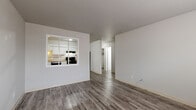 Located at 1134 Westmoreland Rd in Colorado Springs, CO, this single-floor unit offers a clean, updated interior with a consistent design throughout. Wide-plank, wood-look flooring in a warm gray tone runs throughout the entire space, lending a cohesive and modern feel.

The living area is open and well-proportioned, connecting directly to the kitchen via a distinctive pass-through window framed in white — a practical architectural detail that enhances the sense of openness between spaces. The kitchen is well-appointed with white shaker-style cabinetry extending to the ceiling, light granite-look countertops, and black appliances including an electric range, dishwasher, and refrigerator.

The bedrooms are comfortably sized, each featuring ceiling fans, natural light from windows with blinds, and baseboard heating units for efficient warmth. One bedroom includes a built-in closet with bi-fold doors. A hallway connects the sleeping areas to the bathroom, which features a full tub and shower combination with large-format gray tile surround, a white vanity with a mirrored medicine cabinet, and matching wood-look flooring. The neutral gray and white palette throughout creates a bright, move-in-ready atmosphere suited to a variety of living arrangements.