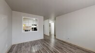 Located at 1134 Westmoreland Rd in Colorado Springs, CO, this single-floor unit offers a clean, updated interior with a consistent design throughout. Wide-plank, wood-look flooring in a warm gray tone runs throughout the entire space, lending a cohesive and modern feel.

The living area is open and well-proportioned, connecting directly to the kitchen via a distinctive pass-through window framed in white — a practical architectural detail that enhances the sense of openness between spaces. The kitchen is well-appointed with white shaker-style cabinetry extending to the ceiling, light granite-look countertops, and black appliances including an electric range, dishwasher, and refrigerator.

The bedrooms are comfortably sized, each featuring ceiling fans, natural light from windows with blinds, and baseboard heating units for efficient warmth. One bedroom includes a built-in closet with bi-fold doors. A hallway connects the sleeping areas to the bathroom, which features a full tub and shower combination with large-format gray tile surround, a white vanity with a mirrored medicine cabinet, and matching wood-look flooring. The neutral gray and white palette throughout creates a bright, move-in-ready atmosphere suited to a variety of living arrangements.