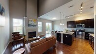 This two-floor home offers a thoughtfully designed layout that balances open communal spaces with functional private areas. A welcoming entryway corridor with rich hardwood flooring and dramatic soaring ceilings leads into the main living area, setting an impressive tone from the moment you arrive. The living room is anchored by a tile-surround fireplace and benefits from abundant natural light streaming through large windows, creating a warm and inviting atmosphere. Tall ceilings throughout the main level add a striking sense of volume and grandeur.

The kitchen is well-appointed, featuring rich dark cabinetry, light granite countertops, stainless steel appliances, and ample storage and prep space. Pendant lighting above the island and track lighting provide layered illumination. The adjacent dining area opens directly to a private outdoor patio through a sliding glass door, creating a seamless indoor-outdoor connection ideal for everyday living and entertaining.

A convenient half bathroom is located on the main level. Carpeted bedrooms on the upper floor offer comfortable retreats, while neutral tones throughout maintain a cohesive, modern aesthetic. The home also includes an attached garage with an automatic opener, providing secure and practical parking and storage.