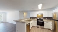 This single-floor residence at 812 Crescent Commons Way in Fayetteville, NC offers a well-designed layout with modern finishes throughout. The kitchen is a standout feature, equipped with white shaker-style cabinetry, granite countertops, a gray subway tile backsplash, and a full suite of stainless steel appliances including a refrigerator, electric range, and dishwasher. A peninsula with an overhang provides additional prep space and casual seating. Light wood-look flooring runs through the kitchen and living areas, complementing the bright, neutral color palette. The spacious living room benefits from natural light through a large window dressed with plantation shutters and features a ceiling fan and a decorative built-in column with open shelving that adds architectural character. The bedrooms are carpeted for comfort and each include ceiling fans. The primary bedroom connects to a private bathroom featuring a granite-topped vanity, white cabinetry, and a soaking tub with a curved shower rod. A second bathroom mirrors the same refined finishes with a granite vanity and wood-look flooring. Clean white walls and consistent trim work throughout give the entire space a cohesive, move-in-ready feel.