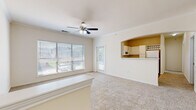 This single-story, one-bedroom, one-bathroom residence offers a thoughtfully arranged floor plan that maximizes comfort and functionality. The spacious living room is a welcoming centerpiece, featuring plush carpeting, crown molding, a ceiling fan with light fixture, and large windows that flood the space with natural light. A glass door provides additional brightness and outdoor access. The kitchen connects to the living area through a charming arched pass-through opening, creating an open, airy feel. It is well-appointed with white cabinetry, light countertops, a full suite of white appliances including a refrigerator, electric range, built-in microwave, and dishwasher, along with wood-style flooring and a window for natural light. A pendant light fixture adds a decorative touch near the dining area. The generously sized bedroom features soft carpeting, a ceiling fan, and a window with outdoor views, complemented by access to a dedicated closet. The full bathroom offers a wide vanity with a large mirror, white cabinetry, a combined tub and shower, and wood-style flooring. A separate laundry area with hookups and a water heater rounds out the practical amenities of this well-appointed residence.
