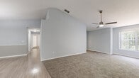 Located in the Compton Estates community of Tampa, FL, this single-story home offers a well-designed, open layout with a consistent soft blue-gray color palette throughout. The spacious main living area is highlighted by dramatic vaulted ceilings, plush carpeting, and a ceiling fan, with a large window that invites natural light and garden views. The kitchen features white cabinetry with dark countertops, a tile backsplash, white appliances including a refrigerator and electric range, and light wood-look flooring. A peninsula breakfast bar opens directly to the dining area, which is accented by a pendant light fixture. The bedrooms are carpeted and well-lit, with ceiling fans and windows overlooking lush greenery; the primary bedroom includes a walk-in closet. The primary bathroom is equipped with a soaking tub, a separate glass-enclosed walk-in shower with decorative tile accents, and light wood-look flooring. A secondary bathroom features a single-sink vanity with dark countertops and a tub/shower combination. A dedicated laundry room accommodates a full-size washer and dryer with overhead shelving. The home offers a practical and comfortable layout suited for everyday living in the heart of Tampa.