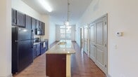 Located at 2120 Waterside Cir in Graham, North Carolina, this single-floor residence offers a thoughtfully designed open-concept layout with stylish finishes throughout. The kitchen serves as the heart of the home, featuring a generous granite-topped island with a built-in sink and pendant lighting overhead, dark espresso cabinetry, matching granite countertops, and black appliances. Hardwood-style flooring flows through the kitchen and main living areas, adding warmth and continuity to the space.

The expansive living area benefits from soaring ceilings, a ceiling fan, and a wall of large windows with transom panes above, flooding the room with natural light. A private door provides direct access to an outdoor balcony, extending the living space outward.

The bedrooms are carpeted for comfort and each features a ceiling fan and natural light from well-placed windows. The primary bedroom connects to a walk-in closet and an en-suite bathroom finished with granite countertops, dark cabinetry with brushed nickel hardware, a large mirror, and a shower/tub combo. A second bathroom mirrors this refined aesthetic with similar granite and cabinetry details. The layout also includes a dedicated walk-in closet, enhancing storage throughout the home.
