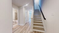 Located at 1801 Guilford Ave in Baltimore's Midtown neighborhood, this thoughtfully designed three-bedroom, four-bathroom home spans three floors, offering a well-organized layout with generous living space. Light wood-tone flooring flows consistently throughout, complementing the neutral, warm white walls that create a bright and clean aesthetic across every level.

The main floor features an open-concept kitchen and living area filled with natural light from large windows. The kitchen is a standout, showcasing a two-tone design with dark lower cabinetry, white upper cabinets, a classic subway tile backsplash, stainless steel appliances, and a large center island with a white countertop, undermount sink, and pendant lighting above.

A convenient half bath with wood flooring and brushed gold fixtures is also found on this level. The hallways are well-lit with recessed lighting, and a staircase with a dark handrail connects all three floors. One of the full bathrooms features floor-to-ceiling neutral tile surrounding a soaking tub, while another half bath offers a minimalist design with a wall-mounted sink.

The three bedrooms are spread across the upper floors, each with light wood flooring. The primary bedroom is a comfortable retreat, while secondary bedrooms offer views of the surrounding Baltimore streetscape through large windows with ceiling fans for added comfort.